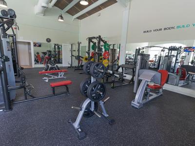 Moderner Fitnessraum mit Kraftgeräten, Hanteln und Spiegeln in einem hellem Raum.