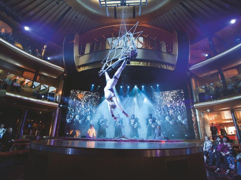 Circus acrobat performs aerial act over stage in elegant theater hall.