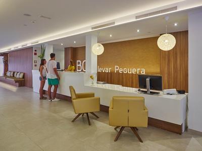 Modern hotel reception area with two people at the counter and wood paneling.