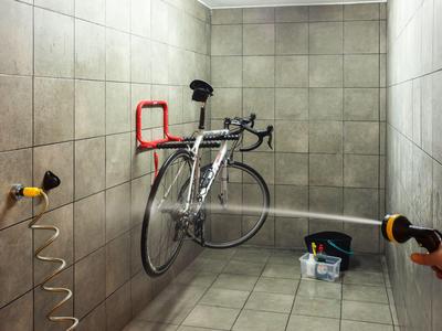Bicicleta asegurada en una habitación con azulejos, con soportes de pared y material de limpieza.