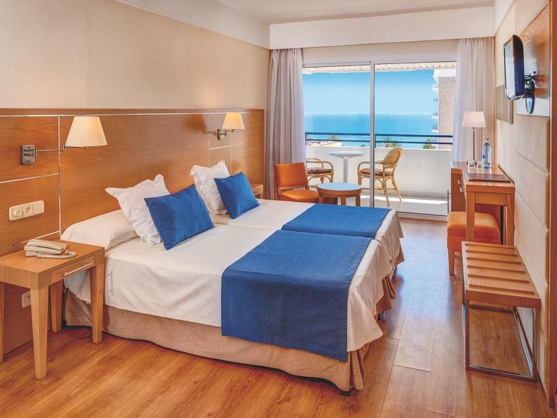 Hotel room with double bed, wooden floor, and balcony overlooking the sea.