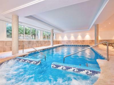 Krytý bazén se spa, sloupy a měkké osvětlení, moderní a relaxační atmosféra.