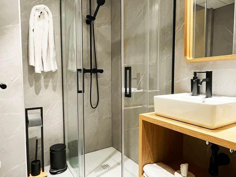 Moderne hotel douche met glazen deuren, zwarte douchekop en stijlvolle wastafel met houten plank.