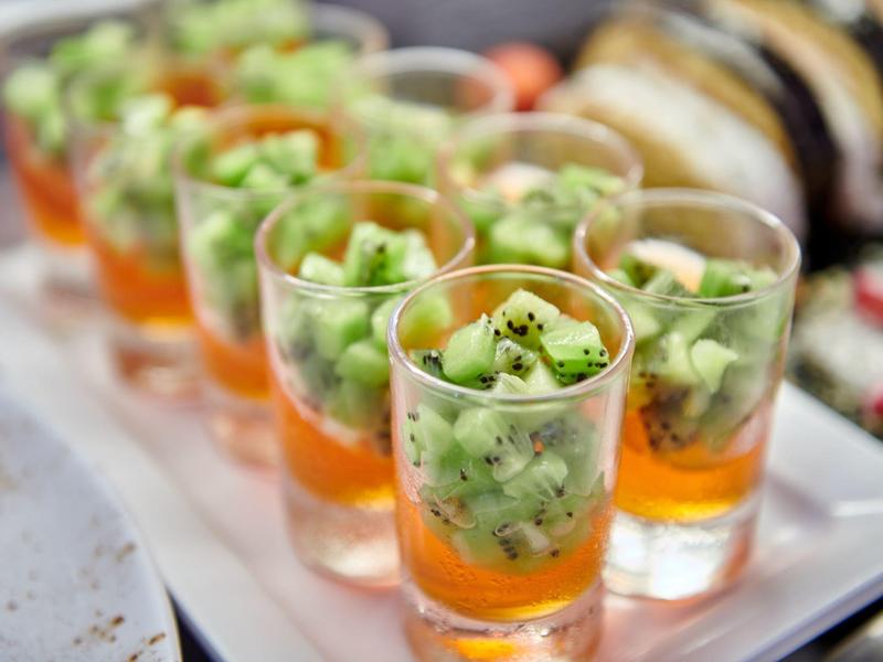 Row of appetizers in small glasses with green vegetables and orange sauce.
