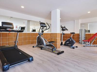 Gimnasio moderno con cinta de correr, máquinas elípticas y banco de pesas en un espacio luminoso.