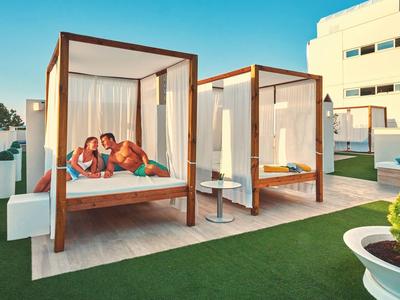 Two cozy canopy beds on a terrace with artificial grass in front of a hotel building in sunlight.