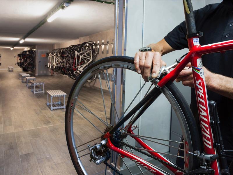 Person repairing a red bike in a bike room with many other bikes on the wall.