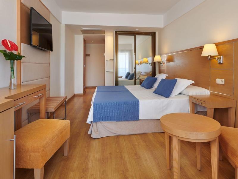 Modernes Hotelzimmer mit Doppelbett, Holzmöbeln, blau-weißer Bettwäsche und warmem Licht.