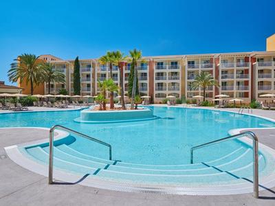 Large swimming pool in front of a multi-story hotel building under clear sky.