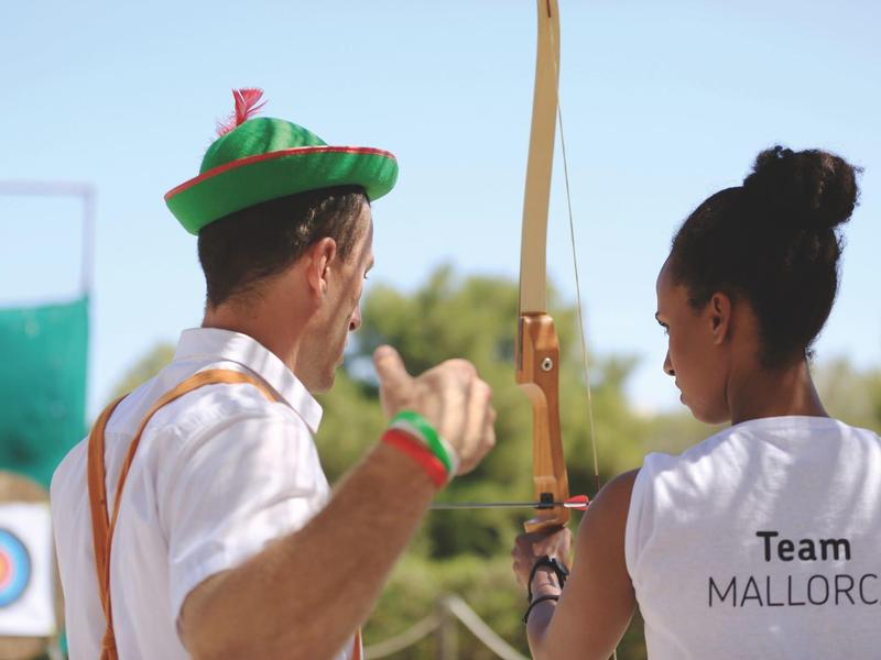 People practicing archery outdoors with a target in the background.