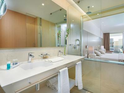 Bright bathroom with sink, mirror, and view into the bedroom.