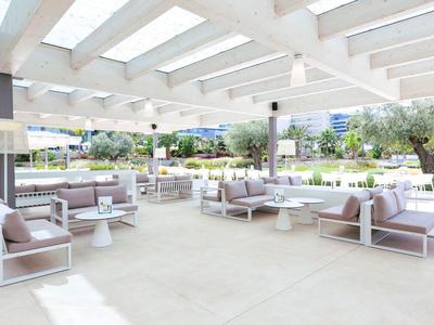 Bright covered outdoor terrace with white furniture and sofas in a hotel garden.