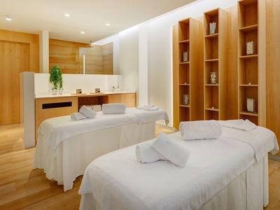 A peaceful spa room with two massage tables, wooden shelves, and warm lighting.
