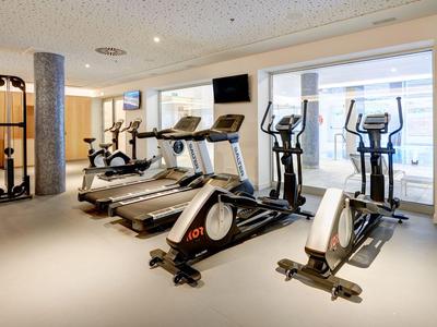 Heller Fitnessraum mit Laufbändern, Fahrrädern und Crosstrainern vor großen Fenstern.