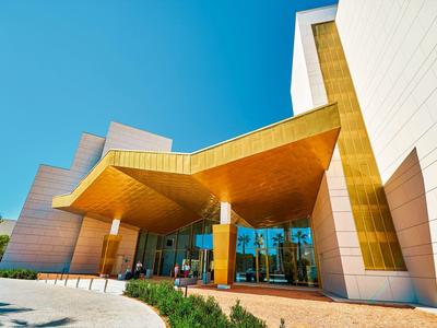 Modern hotel entrance with gold-colored canopy and large glass windows under a clear sky.