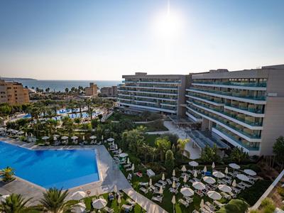 Großer Hotelkomplex mit Pool, Liegestühlen und Blick auf das Meer bei Sonnenuntergang.