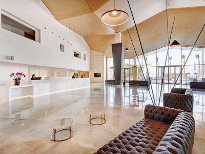 Helle, moderne Hotellobby mit braunen Sofas, weißen Empfangstresen und großen Fenstern.