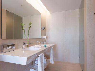 Bright bathroom with double sink and two green plants by the mirror.