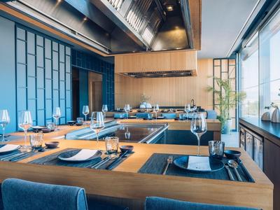 Moderní hotelová restaurace s dřevěnými stoly připravenými k jídlu u velkých oken.