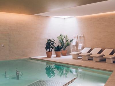 Indoor pool with lounge chairs, plants, and soft overhead lighting in a serene setting.