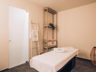Minimalist massage room with white table, towels, wooden ladder, and shelf with decor.