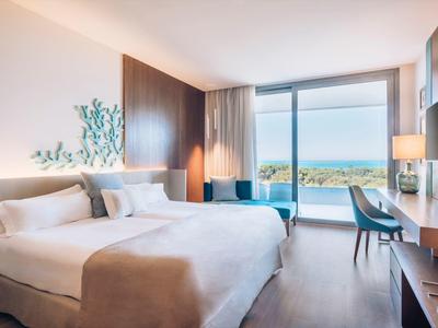 Bright hotel room with large bed, balcony, and sea view.