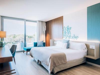 Modernes Hotelzimmer mit großem Bett, Schreibtisch und Blick auf die Natur.