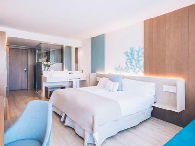 Bright hotel room with a large bed, blue chair, wooden accents, and a modern vanity area.