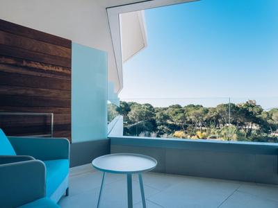 Modern balcony with blue chair, white round table, overlooking green treetops under clear sky.