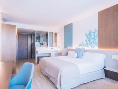Bright hotel room with a large bed, blue chair, wooden accents, and modern decor.