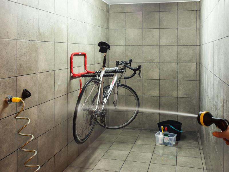 Bicycle awaits maintenance or cleaning in a narrow tiled room with wall-mounted holders.
