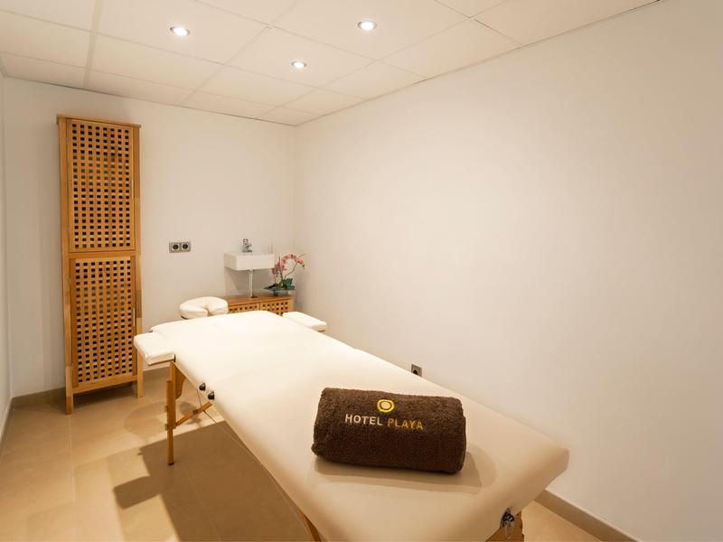 A serene massage room with a white massage table and a dark brown hotel pillow.