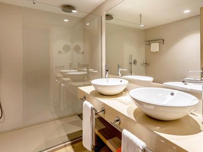 Modern bathroom with two white sinks, large mirrors, and spacious shower area.