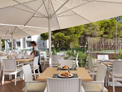 Outdoor restaurant with white chairs and tables under umbrellas, waiter serving guests.