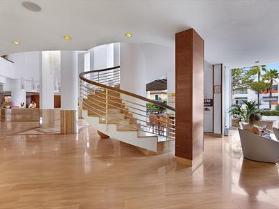 Bright hotel lobby with spiral staircase and seating areas by large windows.