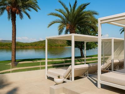 Modern hotel terrace with white beds, palm trees, and a calm lake view on a sunny day