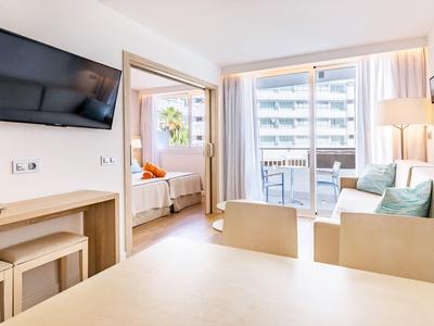 Bright hotel room with seating area, TV, and balcony with city view.