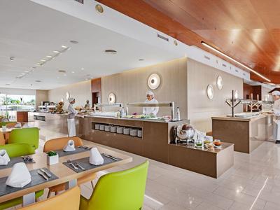 Bright restaurant with modern design, green chairs, and set tables in a hotel.