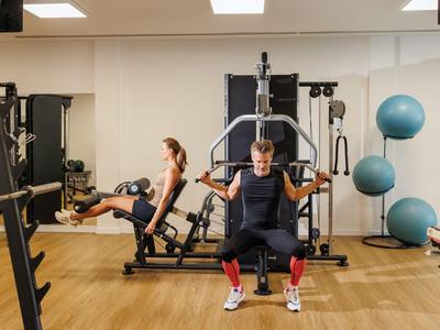 Dos personas haciendo ejercicio en un gimnasio luminoso con varios equipos y grandes pelotas de ejercicio.
