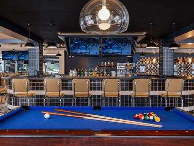 Modern bar with blue pool table, stools, and dark ceiling with large lights
