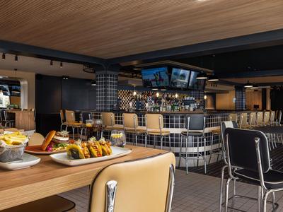 Moderner Hotelbarbereich mit Holztisch, bequemen Stühlen und einem Tresen mit Barhockern.