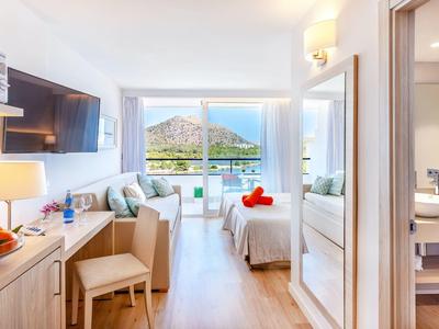 Bright hotel room with sea and mountain view, modern furnishings, and bathroom.