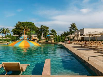 Large pool with colorful water play area surrounded by loungers and umbrellas under blue sky