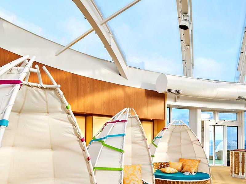 Indoor lounge area with white hammock chairs, colorful pillows, round tables, and green carpet.