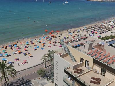 Uitzicht op een druk zandstrand met kleurrijke parasols en een hotelgebouw op de voorgrond.
