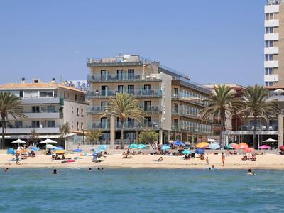 Zandstrand met parasols en mensen voor hotels en palmbomen aan zee.