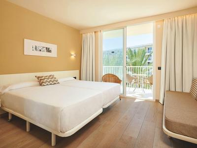 Helles Hotelzimmer mit Doppelbett, Balkon und Sitzbereich in warmen Tönen.