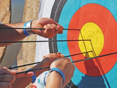Several hands are drawing arrows on a colorful target board.