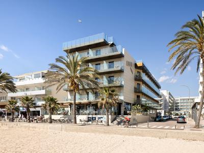Modernes Hotel mit Terrassen und Palmen direkt am Sandstrand bei blauem Himmel.