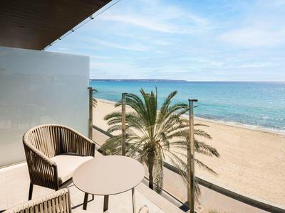 Balkon mit Stuhl und Tisch mit Blick auf Sandstrand, Palmen und Meer unter blauem Himmel.